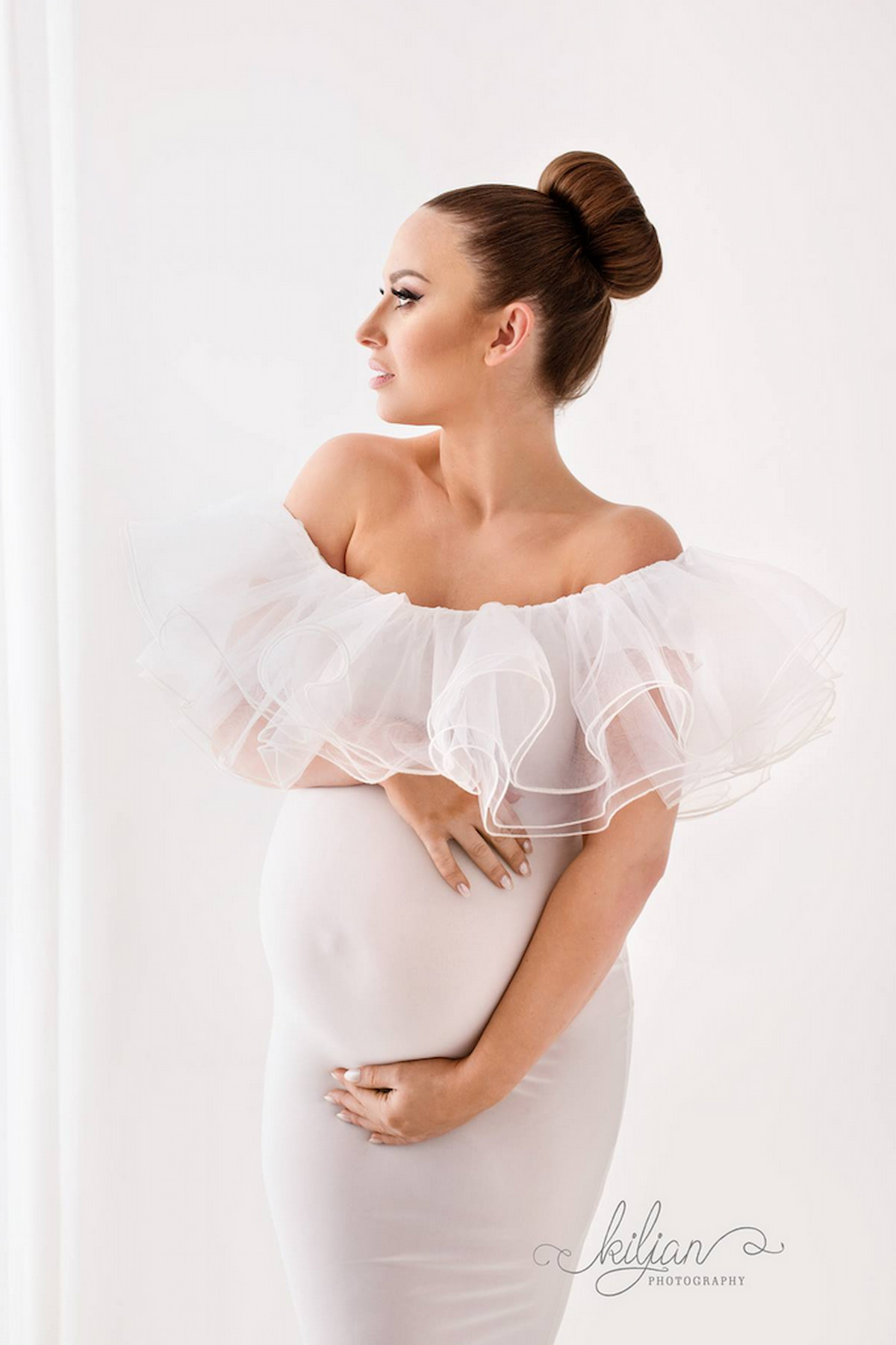 Pregnant woman in elegant off shoulder gown with voluminous tulle neckline, studio portrait