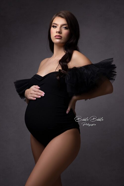 Pregnant woman in black Scarlett bodysuit with tulle sleeves, elegant studio maternity portrait