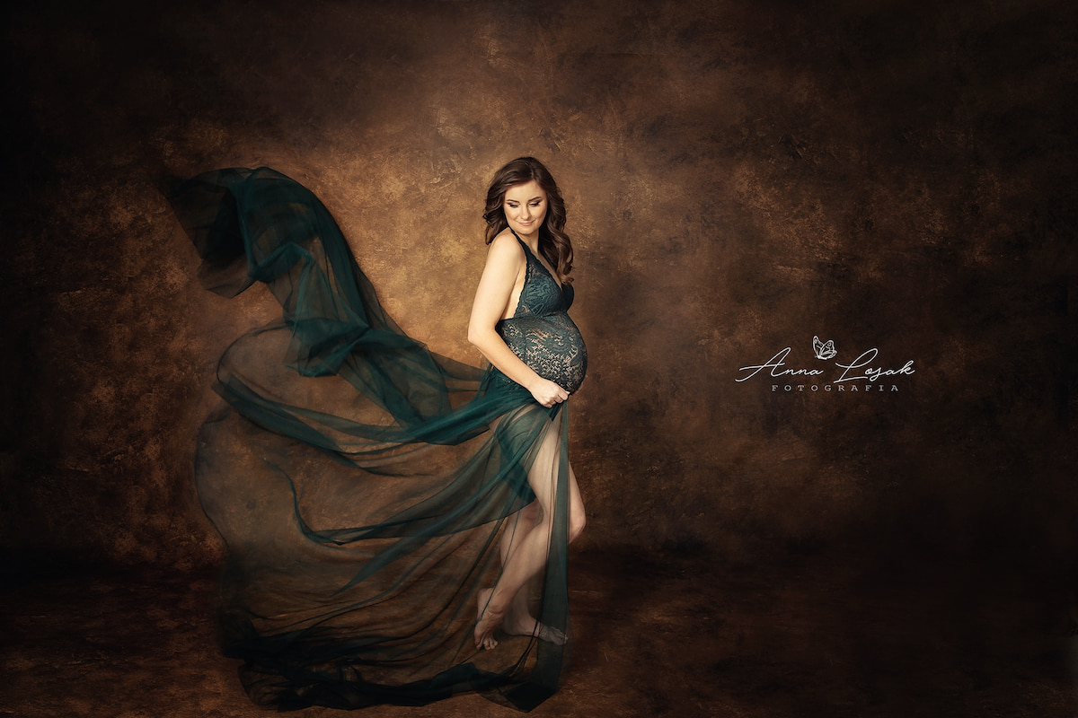 Pregnant woman in green lace Sofia bodysuit with flowing tulle fabric, studio maternity photoshoot