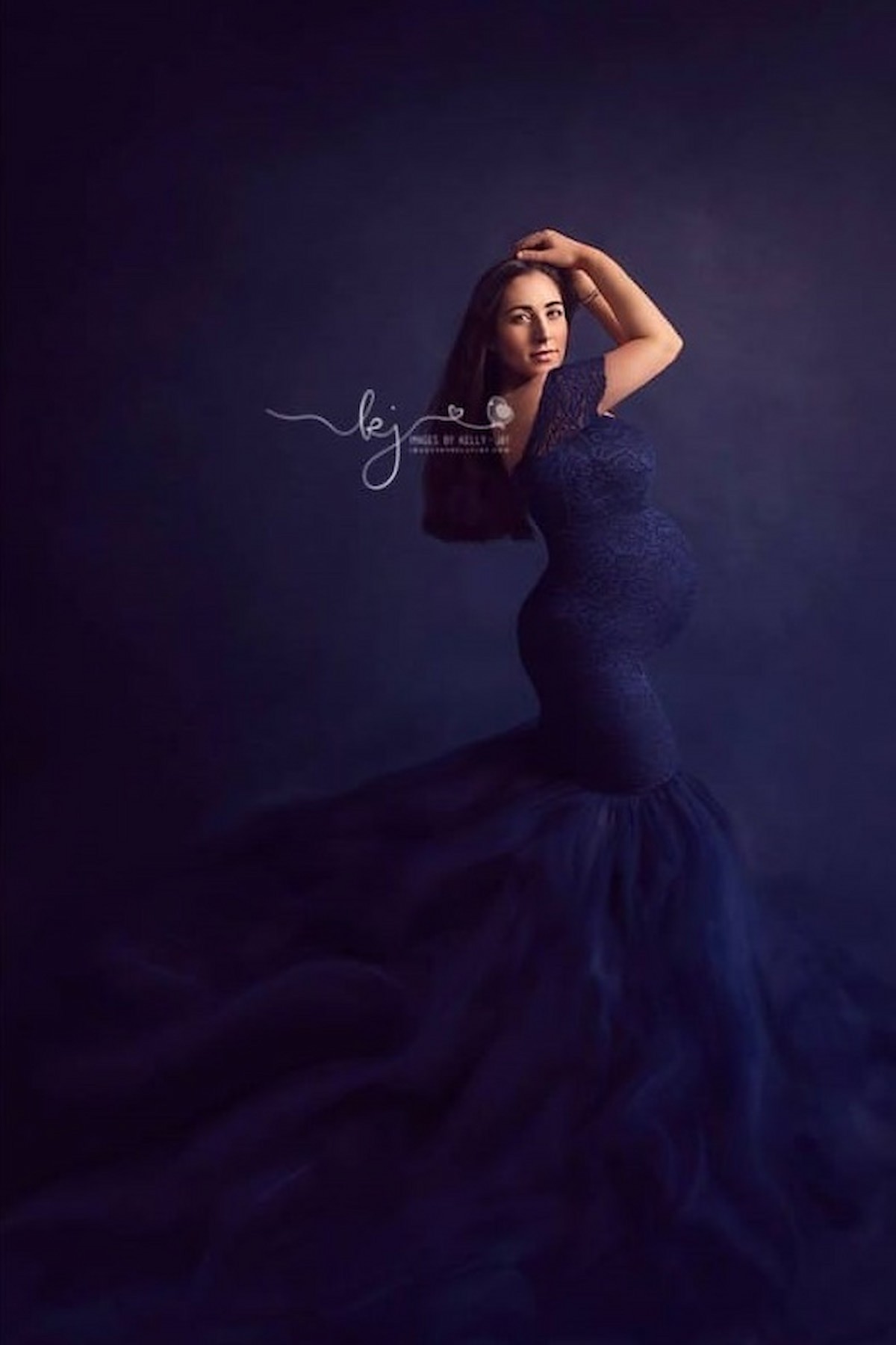 pregnant woman wearing navy lace mermaid maternity dress in studio portrait