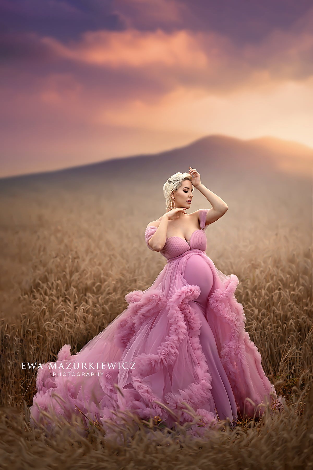 pregnant woman wearing pink tulle maternity gown with ruffled train in wheat field