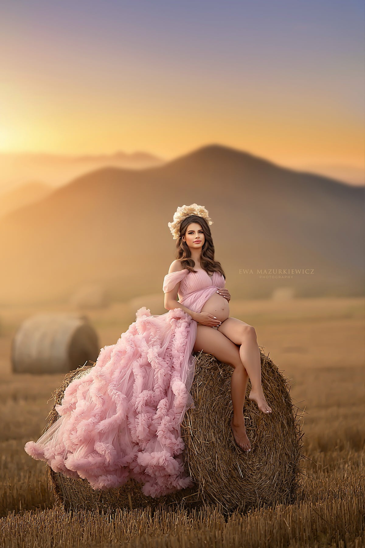 pregnant woman sitting on hay bale wearing flowing tulle maternity gown